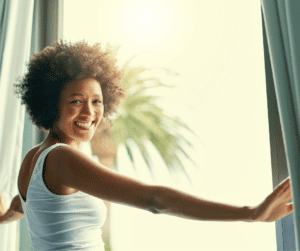 A young woman smiling as she holds curtains apart for the start of a new day.