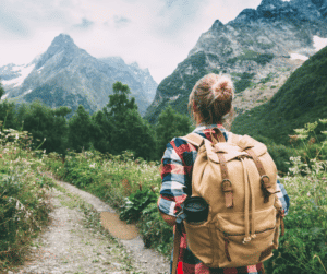 A woman with a backpack walking the path to healing with a mountain to climb ahead of her.