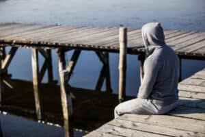 Man sitting on a pier by the water looking out.