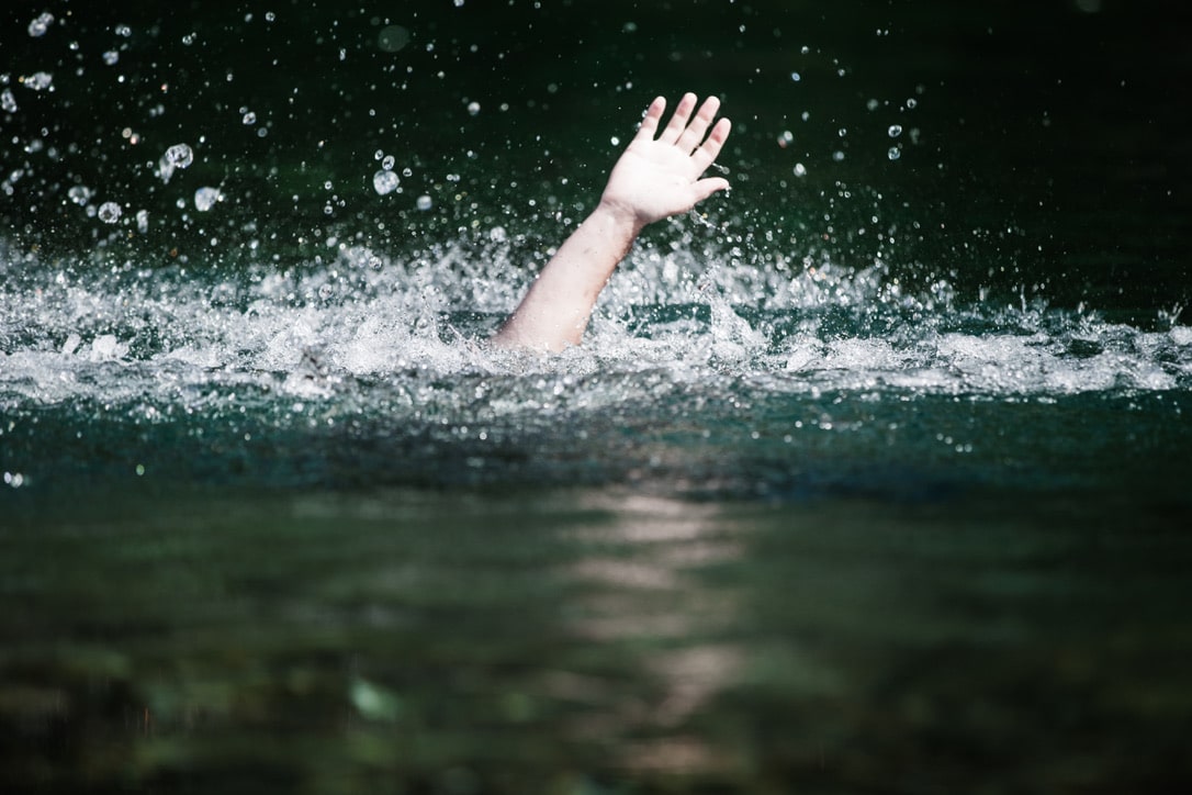 A man who's drowning, waving his hand above the water to ask for help.
