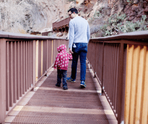 A father holding hands with his child as they walk across a wooden bridge, acting as a safety zone.