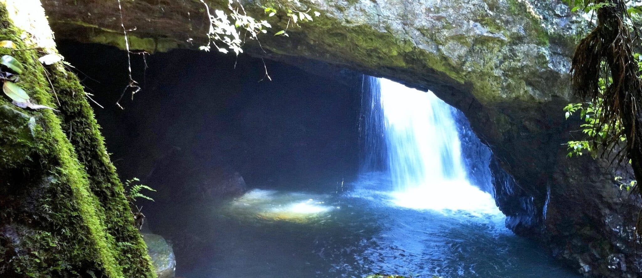 Arch of a natural bridge with water streaming into a pool beneath.