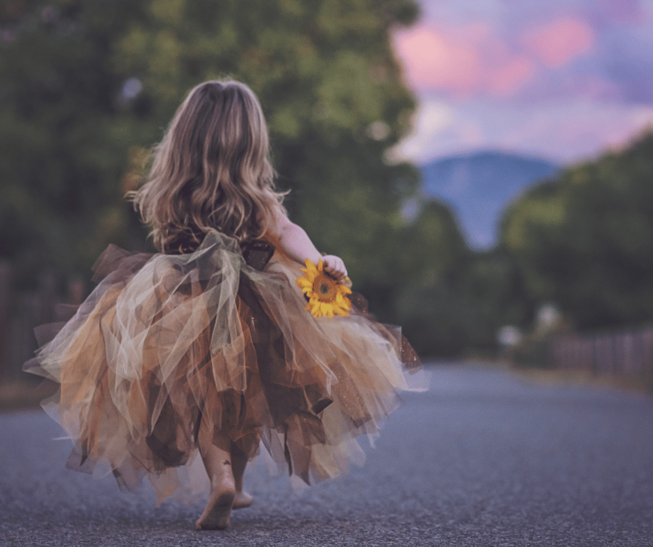 A little girl walking barefoot in a tutu, holding a sunflower and feeling joyful.