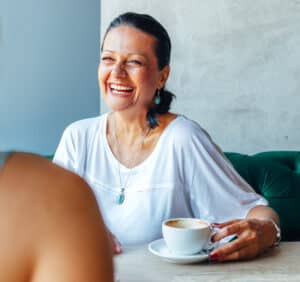 Woman sitting at a table with coffee cup and smiling at another woman .