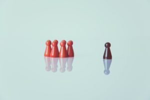 Picture of some little orange people figures standing separate to a brown little person figure.